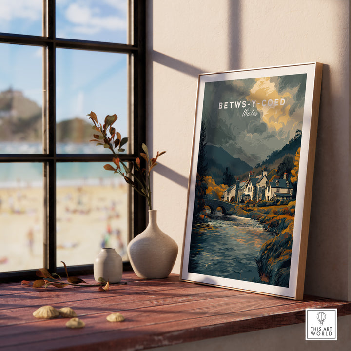 Framed Betws-y-Coed Wales travel poster by a window, showcasing Snowdonia's scenic beauty and charming village.