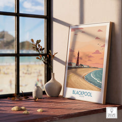 Blackpool Sunset Tower Beach Art Print | Pink Sky UK Coastal Poster displayed on a shelf by a window with beach view.