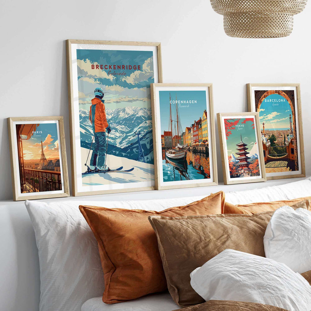 Collection of travel posters featuring Breckenridge, Copenhagen, and Barcelona displayed above a cozy bed with decorative pillows.