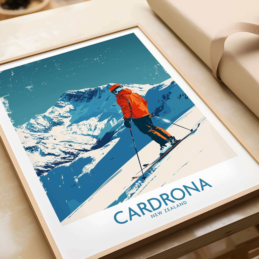 Cardrona Ski Print featuring a skier in an orange jacket against New Zealand's snow-capped mountains. Perfect for ski lovers.