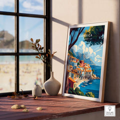 Corsica Wall Art framed on a wooden table with a view of the beach, showcasing vibrant colors and serene landscapes.