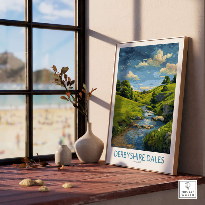 Derbyshire Dales poster art print featuring rolling hills and a stream, displayed on a windowsill.