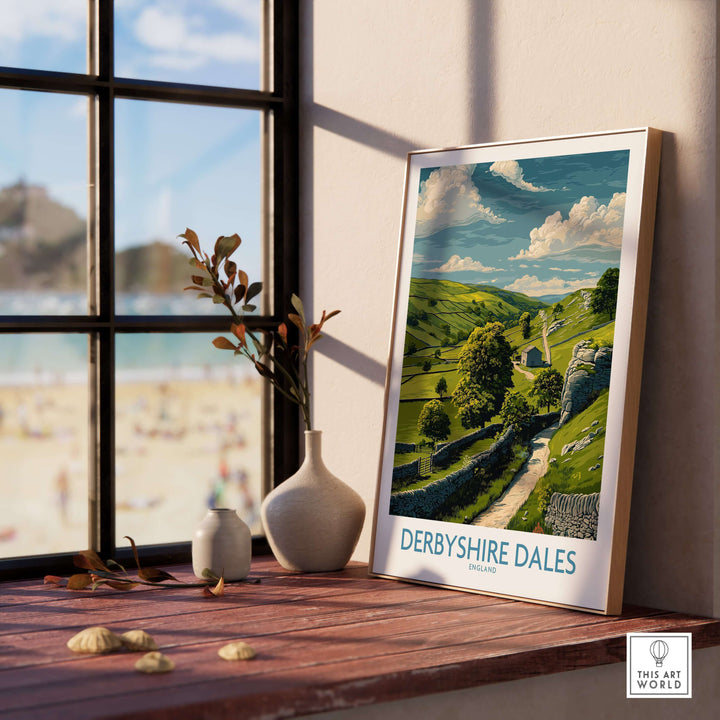 Derbyshire Dales poster showcasing English landscape art, framed on a wooden table near a window.