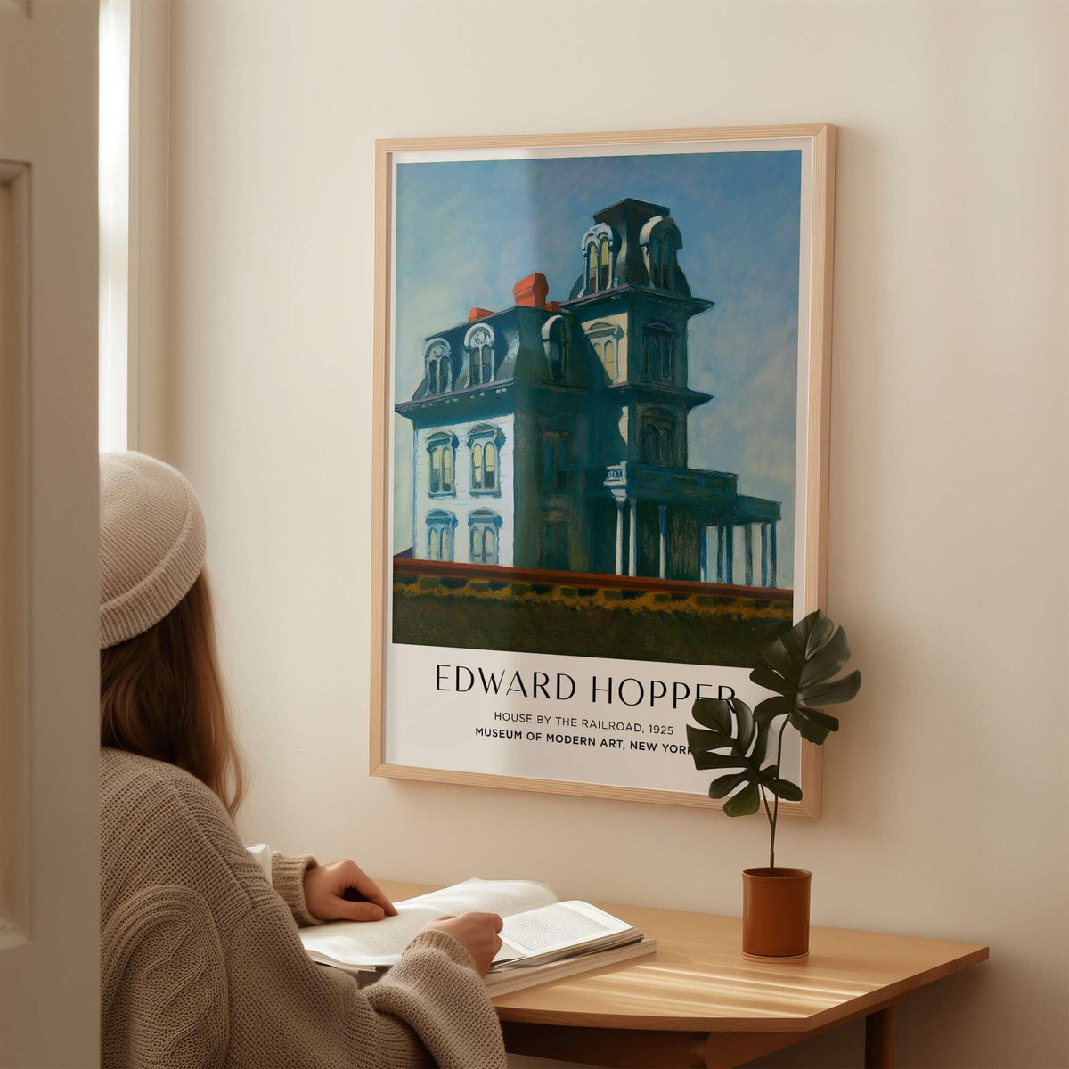 Edward Hopper House by the Railroad 1925 MoMA Art Print Poster displayed on wall above a person reading.