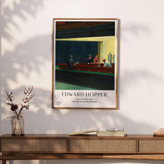 Edward Hopper Nighthawks 1942 Iconic Diner Art Print AIC Poster framed on a wall above a wooden table.