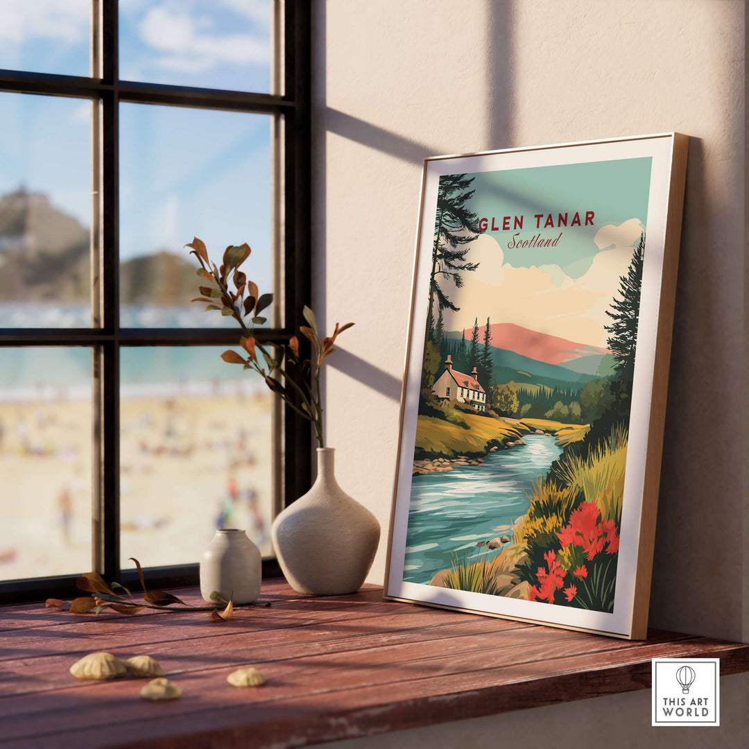 Glen Tanar Scotland poster showcasing a vibrant landscape with mountains and river, displayed on a wooden table near a window.