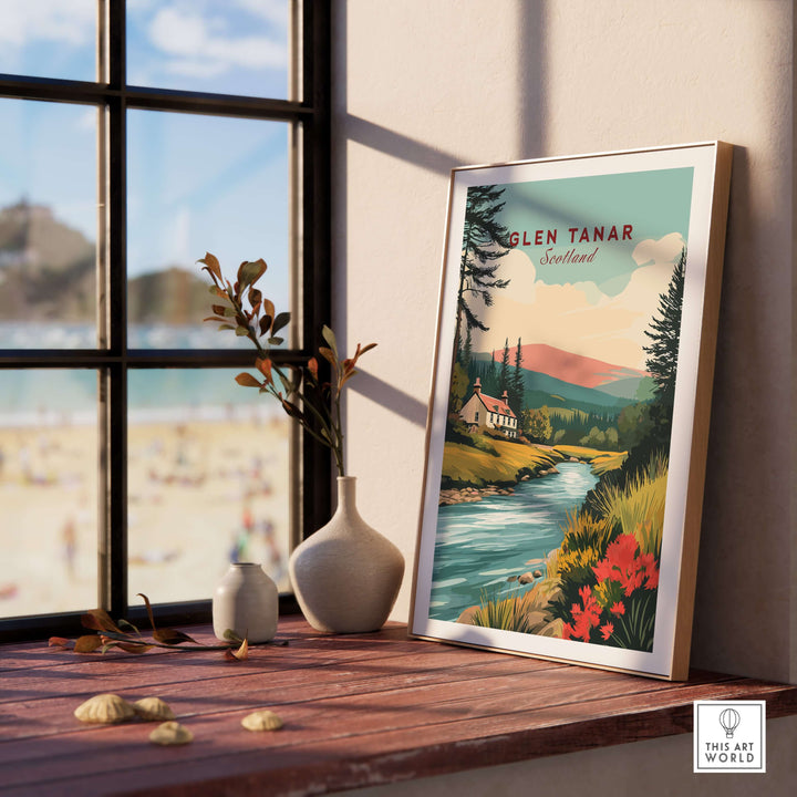 Glen Tanar Scotland poster showcasing a vibrant landscape with mountains and river, displayed on a wooden table near a window.