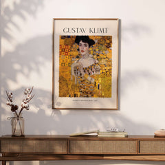 Gustav Klimt Art Print - Portrait of Adele Bloch-Bauer I Poster 1907 framed on a wall above a stylish wooden table.