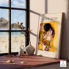 Gustav Klimt Art Print - The Kiss 1907 displayed on a wooden table with a scenic view outside.