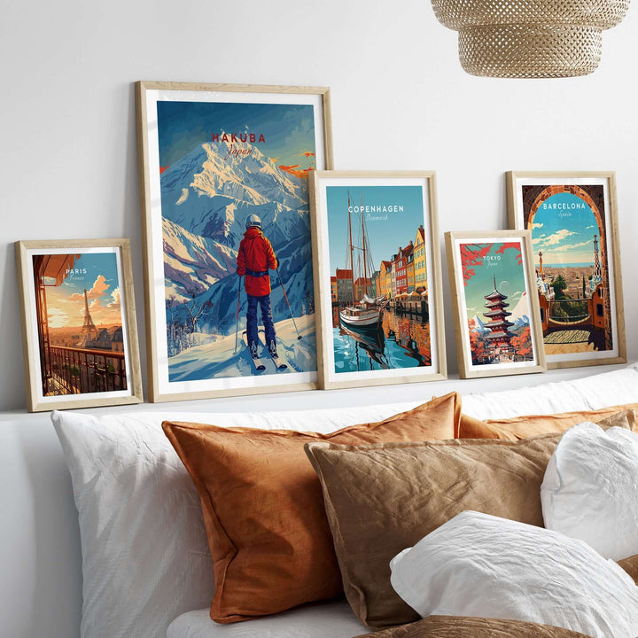 Collection of framed travel posters including Hakuba ski poster displayed above a couch with brown and white cushions.