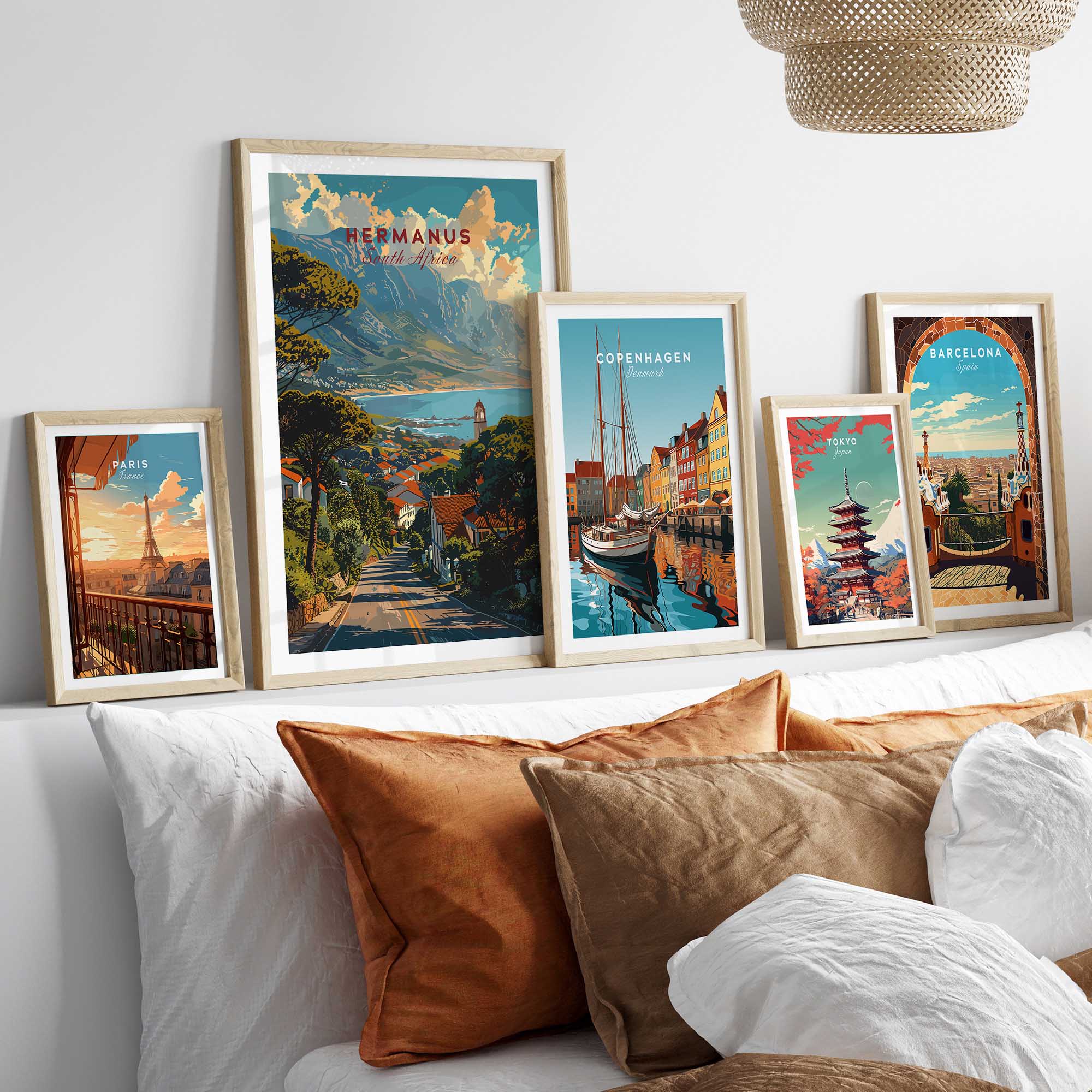 Hermanus Art Print South Africa displayed among travel posters on a styled bed with decorative pillows.