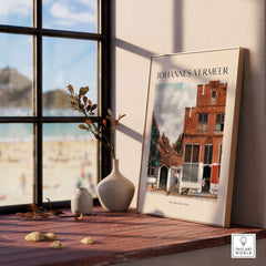 Johannes Vermeer The Little Street 1657 Delft Scene Dutch Golden Age Art Print displayed on a wooden table by a window.