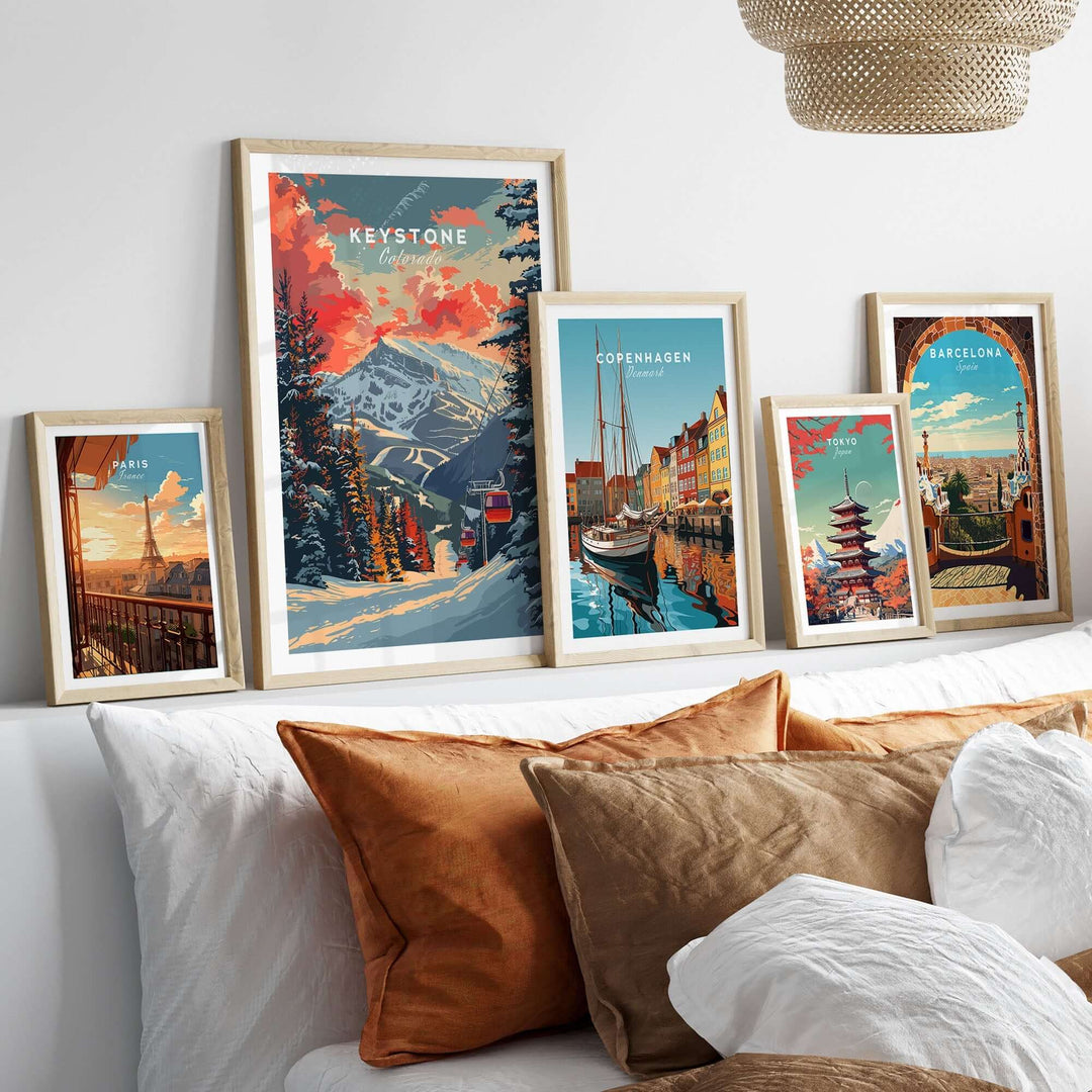 Framed travel posters of Keystone, Copenhagen, and Barcelona displayed on a shelf above a cozy bed with textured pillows.