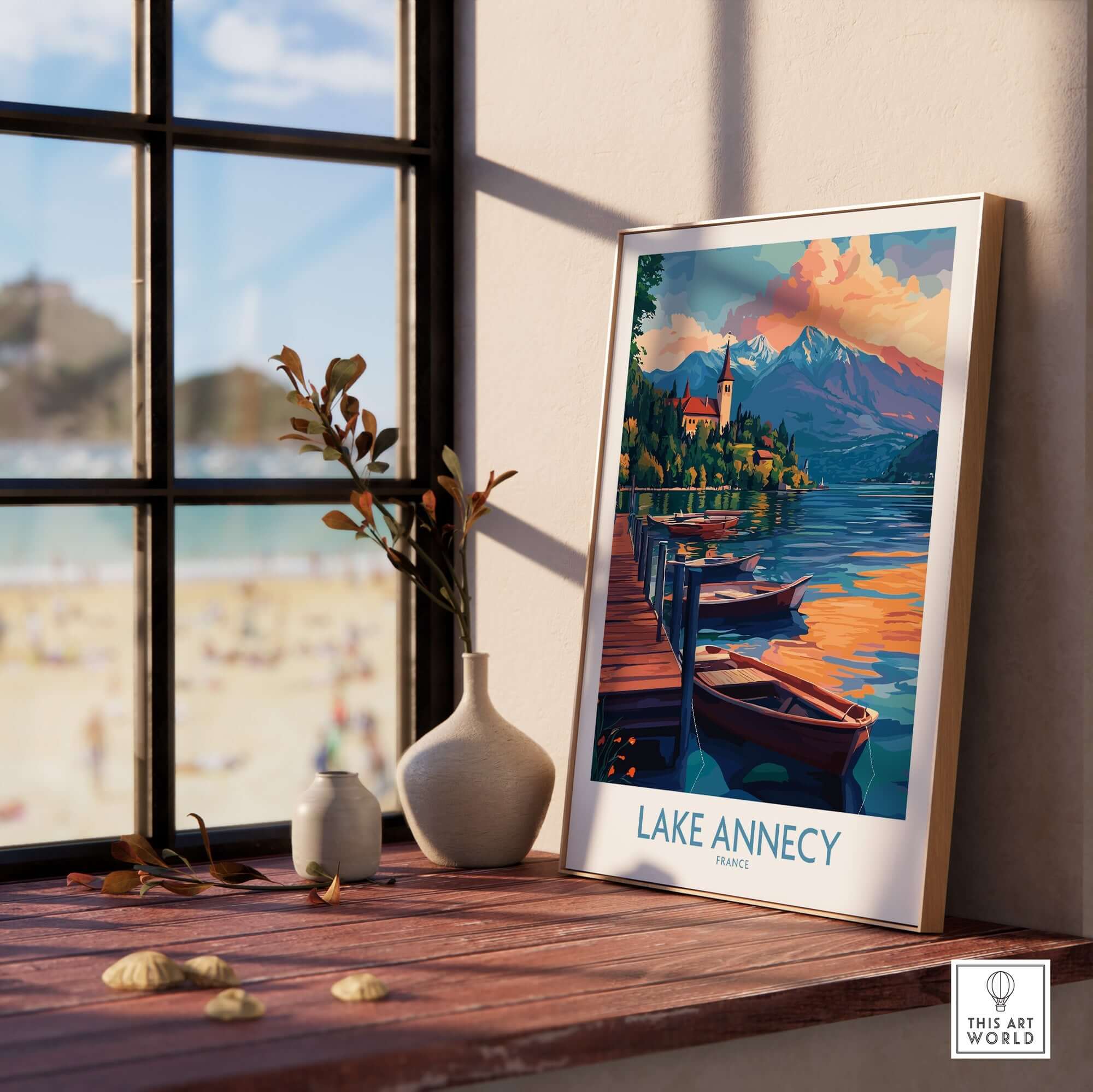 Lake Annecy Wall Art Print displayed on a wooden table by a sunny window with boats and mountains in the background.