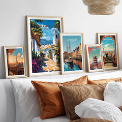 Marbella Wall Art collection displayed above a cozy bed with decorative pillows, featuring travel posters from various cities.