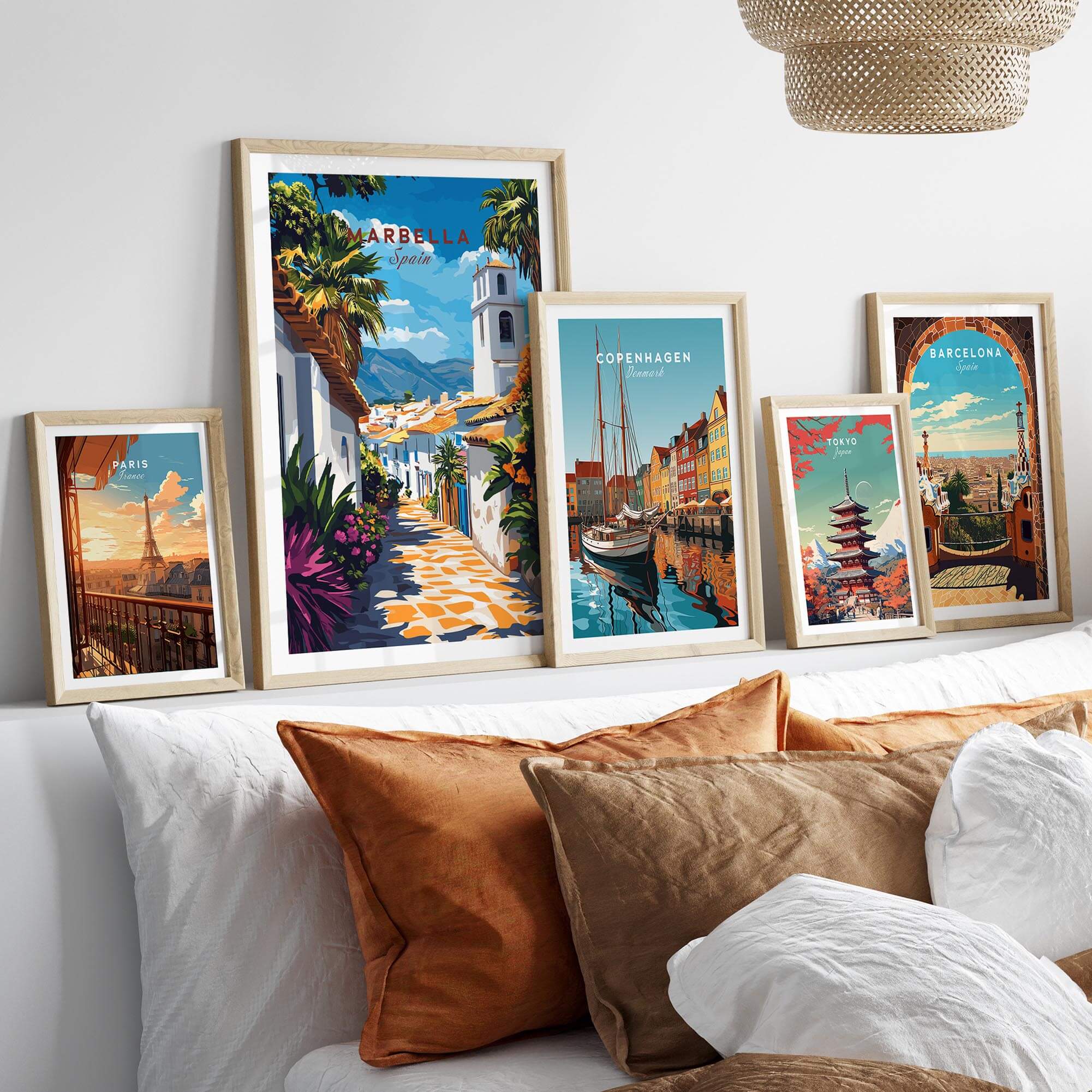 Marbella Wall Art collection displayed above a cozy bed with decorative pillows, featuring travel posters from various cities.