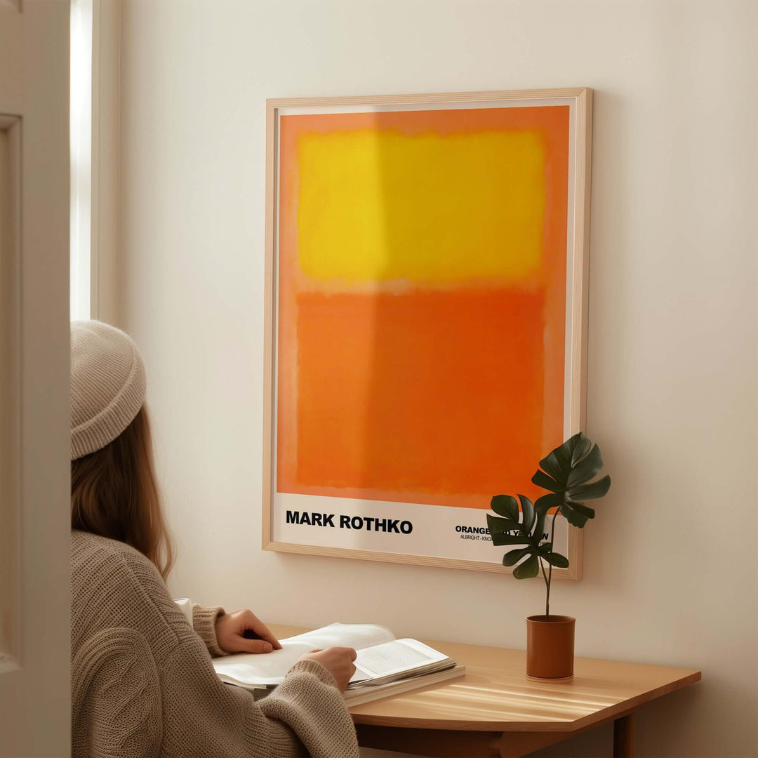 Mark Rothko art print 'Orange and Yellow' (1956) on wall, woman reading at desk, featuring bold color field design.