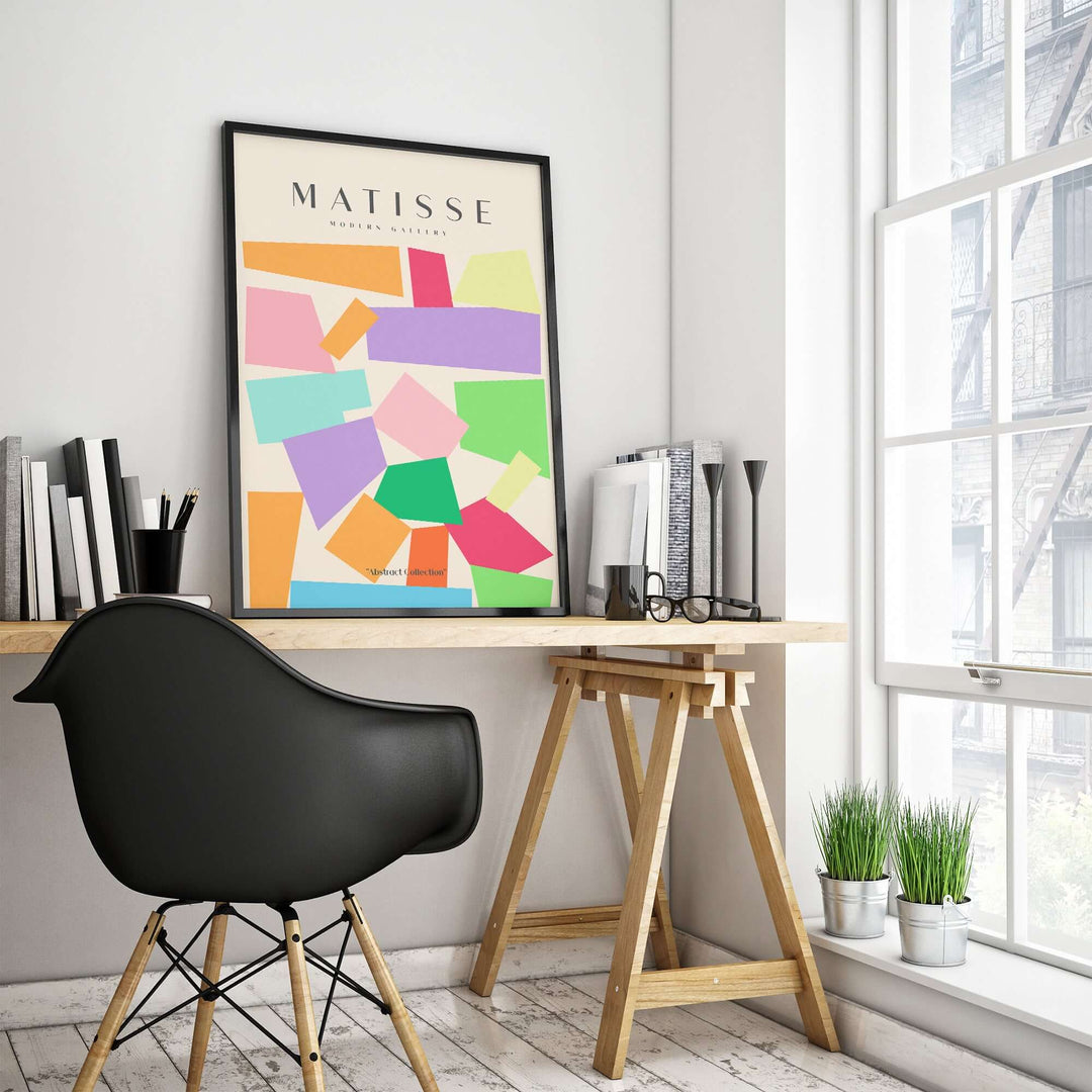 Matisse art print with colorful geometric shapes hanging in a modern workspace with wooden desk and black chair.