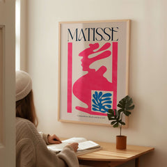 Matisse Art Print Composition Pink Blue Abstract Cut Out Print 1947 displayed on a wall above a person reading.