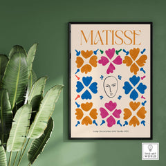 Matisse Art Print - Large Decoration with Masks Floral Pattern Poster displayed on a green wall surrounded by plants.
