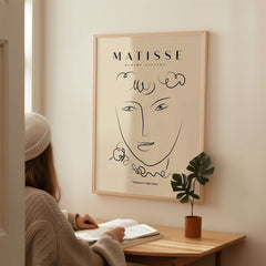 Matisse Art Prints -  Line Art Face Curly Hair Minimalist Poster displayed on a wall above a seated person.