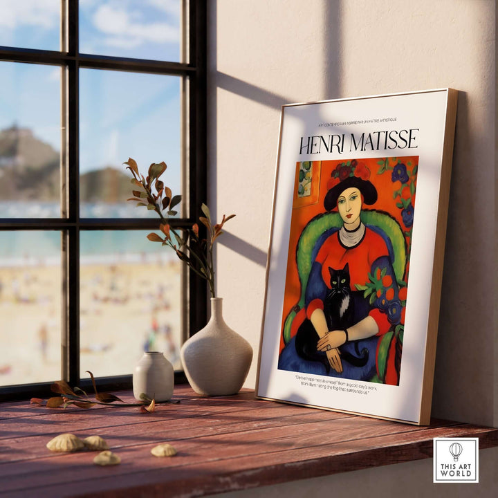 Matisse art print of a woman with black cat in colorful room, displayed on a wooden table with beach view.