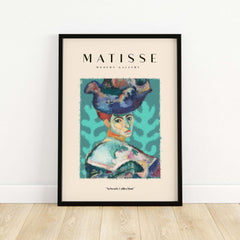 Matisse Art Prints - Woman Large Hat Portrait Teal Background Poster displayed in a modern frame on wooden floor.