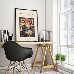 Matisse Art Prints -  Woman in Patterned Hat & Dress Poster displayed in a modern office setting with a stylish chair.
