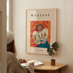 Matisse Art Prints - Woman White Blouse Blue Skirt Portrait Poster framed on wall behind a person reading.