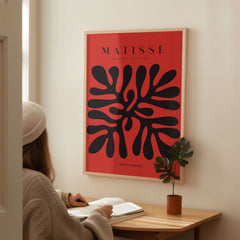 Matisse Art Prints -  Black Abstract Coral Shape Red Poster displayed on wall above a person reading at a desk.
