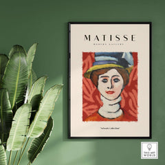 Matisse Art Prints - Woman in Elaborate Hat Portrait Poster displayed in a modern gallery setting with plants.