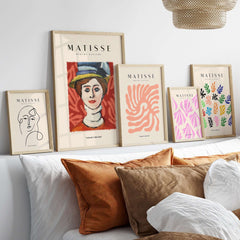 Matisse Art Prints - Woman in Elaborate Hat Portrait Poster displayed on a modern wall above stylish cushions.