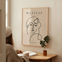 Matisse Art Prints - Continuous Line Abstract Face Poster displayed on a wall beside a seated person studying.