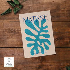 Matisse Cyan Blue Abstract Shape Papiers Découpés Poster on wooden surface with green leaves.