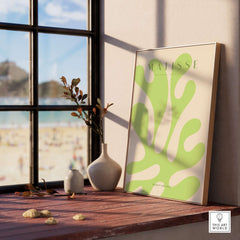 Matisse Art Prints - Lime Green Abstract Coral Shape Poster displayed on a wooden table near a window with beach view.