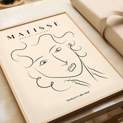 Matisse Art Prints -  Line Art Ladies Face with Wavy Hair Minimalist Poster displayed in a wooden frame against a beige background.