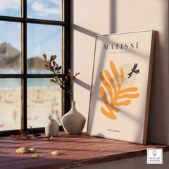 Matisse Art Prints - Orange Leaf Bird Silhouette Poster displayed at a sunlit window with beach view.