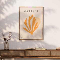 Matisse Art Prints - Orange Seaweed Abstract Art Print displayed on a wall above a wooden table with decorative flowers.