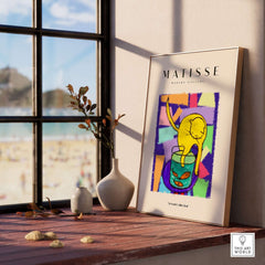 Matisse Art Prints - Yellow Cat with Fishbowl Geometric Poster displayed on a wooden table with a beach view.