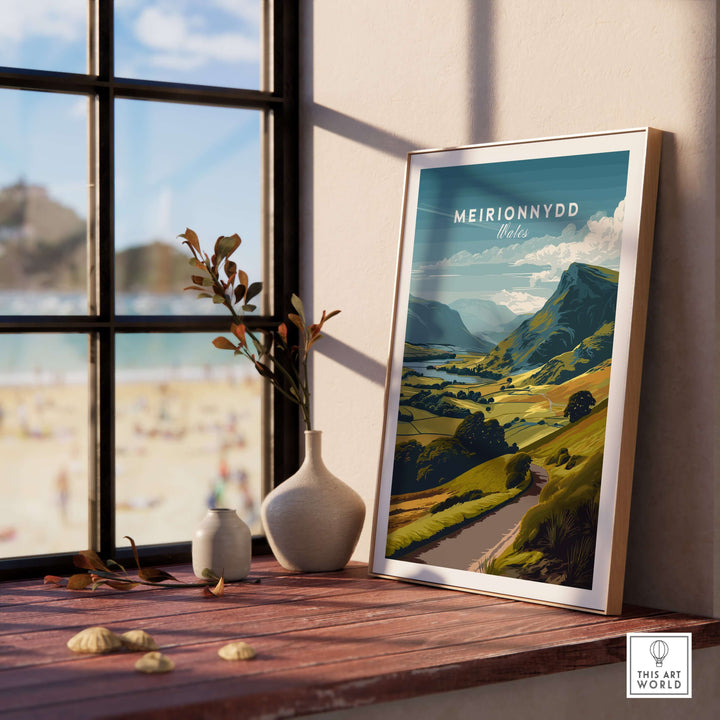 Meirionnydd Wales mountain landscape poster displayed on a sunny windowsill with beach view.