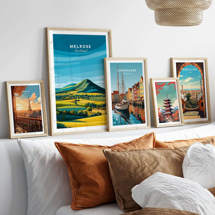 Melrose Scotland travel posters in frames on a stylish bed with decorative pillows, showcasing scenic landscapes.