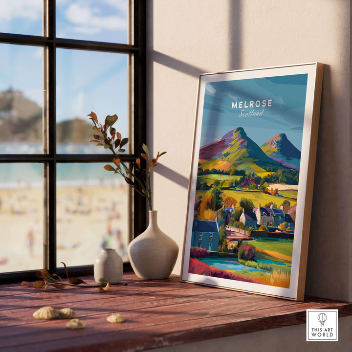 Framed Melrose Scotland travel print featuring Eildon Hills and village houses by a window.