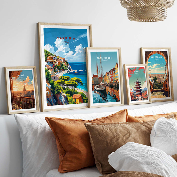 Collection of framed travel posters on a bed, featuring scenic views of Sardinia, Copenhagen, and Barcelona