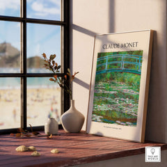 Monet Japanese Footbridge Water Lilies Giverny Garden Poster Art Print displayed on a wooden table beside a window.