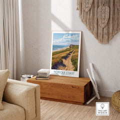 Norfolk Coast Print displayed on a wooden bench in a cozy living room, capturing the serene beauty of the coastline.