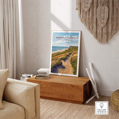 Norfolk Coast Travel Poster displayed in a cozy living room with natural decor and wooden furniture.