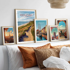 Norfolk Coast Travel Poster displayed among other travel posters on a cozy sofa with decorative pillows.
