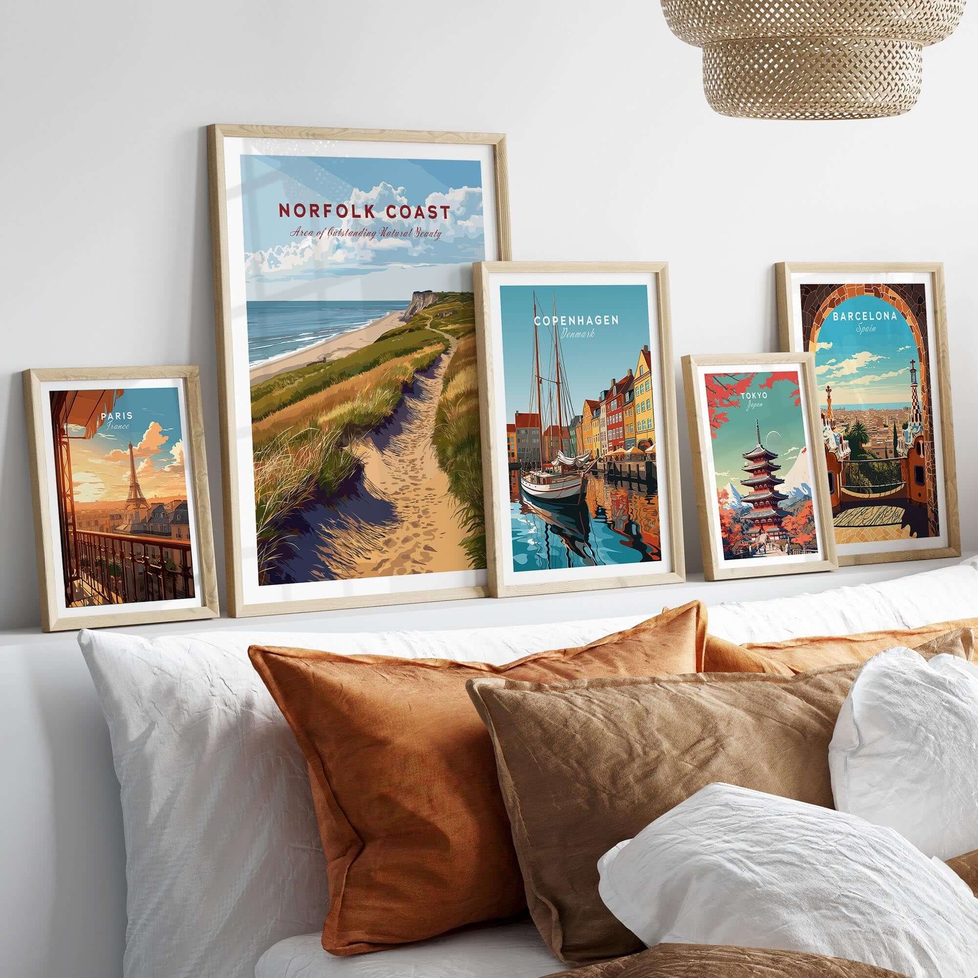 Norfolk Coast Travel Poster displayed among other travel posters on a cozy sofa with decorative pillows.