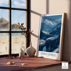 Orient Express Print | Snowy Mountain Poster displayed on a tabletop near a window with a beach view.