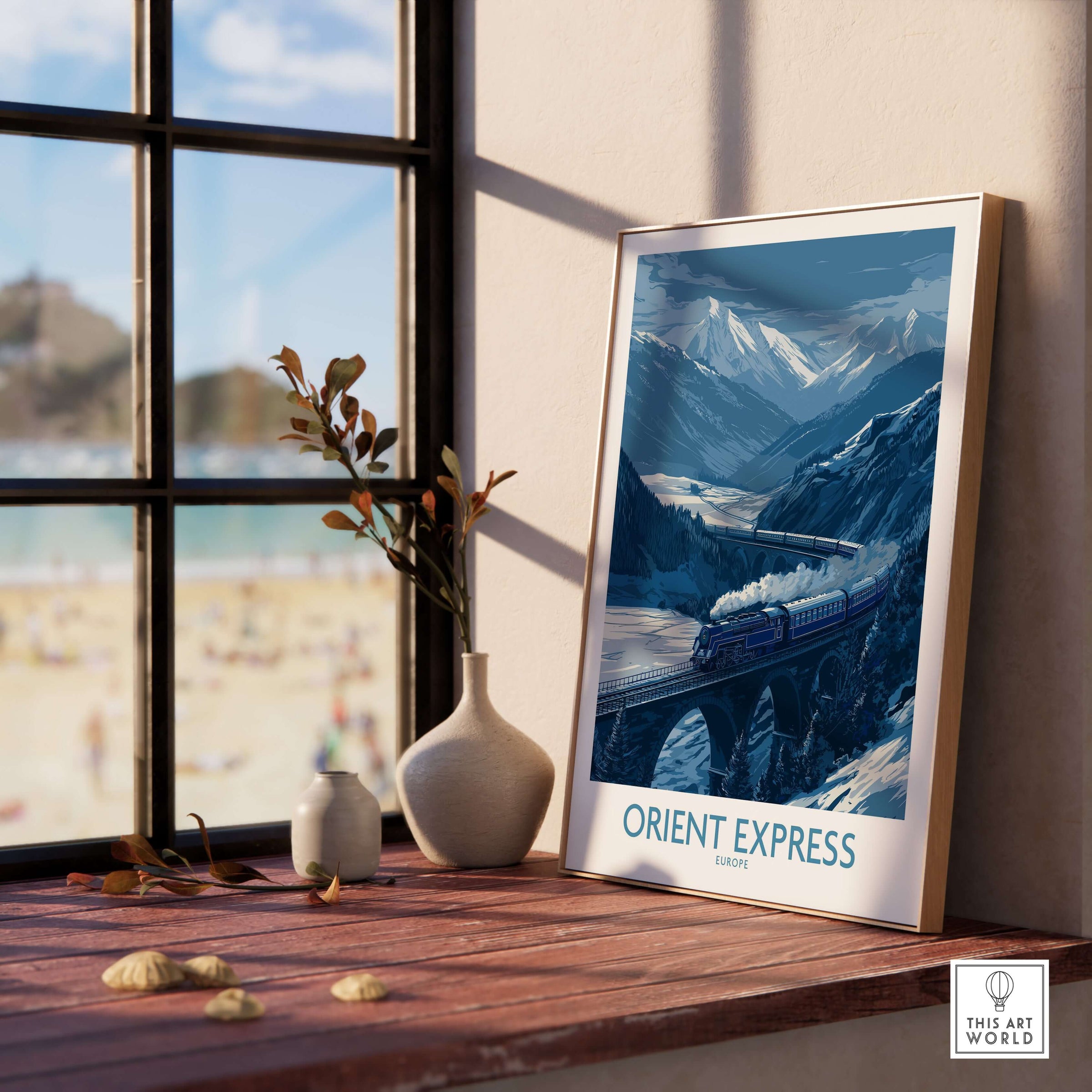 Orient Express Print | Snowy Mountain Poster displayed on a tabletop near a window with a beach view.